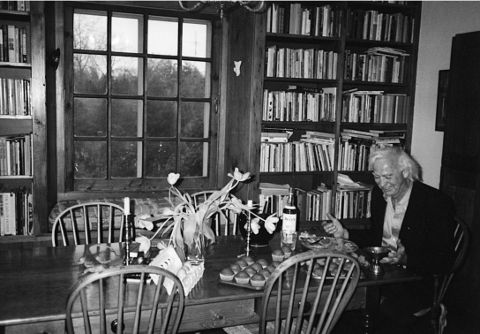 Leon Rooke sitting at a table next to full bookshelves